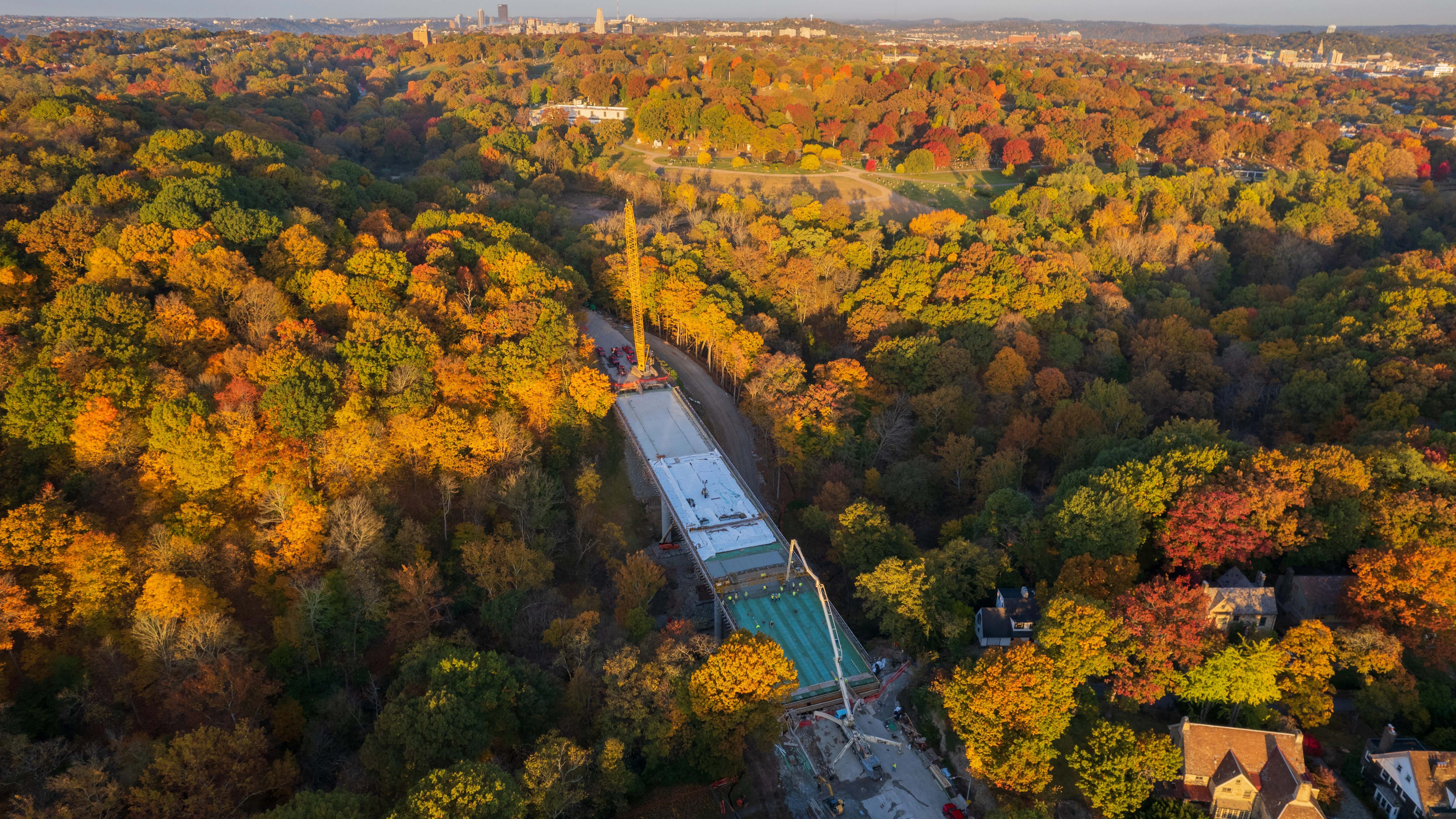 An image of the bridge deck being placed during the rebuilding of the Fern Hollow Bridge with the colors of fall dotting the landscape surrounding the bridge